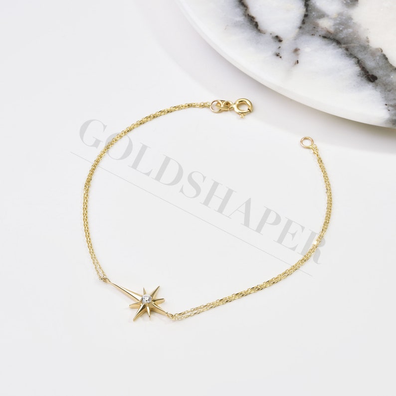 May include: A gold chain bracelet with a star charm featuring a small clear stone in the center.