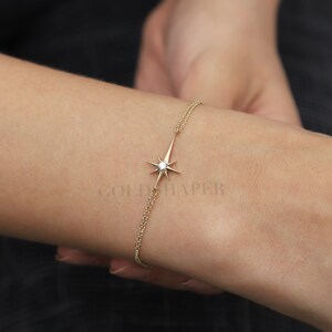 May include: A delicate gold chain bracelet with a star-shaped pendant featuring a small diamond in the center. The bracelet is on a person's wrist.
