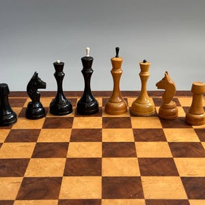 以下が含まれることがあります： チェスボードの上に一列に並べられた10個の木製チェス駒。黒い駒5個と明るい茶色の駒5個のセットで、ポーン、ナイト、クイーン、キングなど、それぞれ異なる形状の頂部を持つ駒が含まれています。