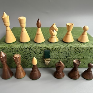 May include: A chess set featuring wooden pieces in light and dark shades, displayed on a green textured box. The set includes pawns, rooks, knights, bishops, a queen, and a king. The box has a green leather-like texture and a brass clasp.