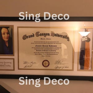 May include: A framed diploma from Grand Canyon University for Natalie Denise Robinson, with a graduation tassel in purple and orange. The diploma is in a black frame with a white mat. The frame has a small photo of a woman in a cap and gown, and the text "Keep dreaming & Make reality" below the photo.