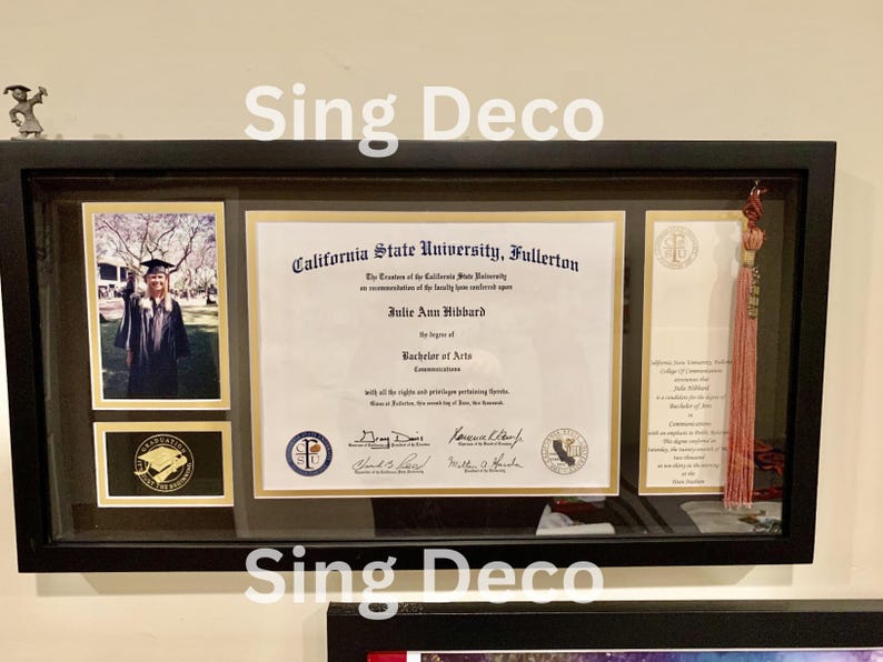 May include: A framed diploma from California State University, Fullerton, awarded to Julie Ann Hibbard for a Bachelor of Arts in Communications. The diploma is displayed with a graduation photo and a tassel.