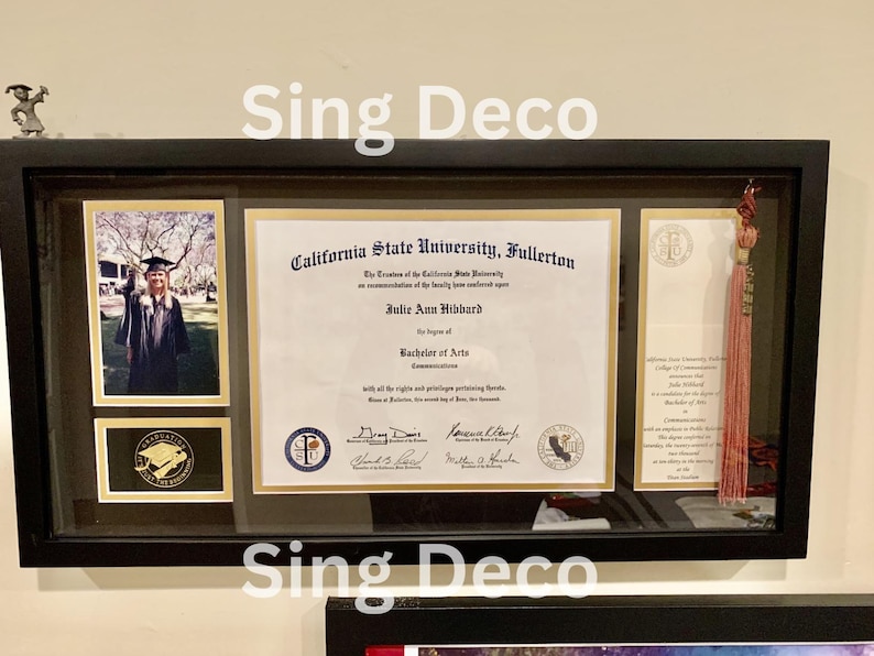 May include: A framed diploma from California State University, Fullerton, awarded to Julie Ann Hibbard for a Bachelor of Arts in Communications. The diploma is displayed with a graduation photo and a pink tassel.