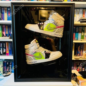 May include: A pair of high-top sneakers in a black framed display. The sneakers are white with gray, black, and neon green accents. The design includes a pixelated green swoosh and the text "SHOE BOY".