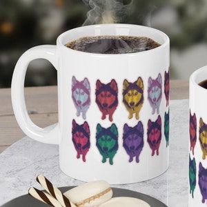 Può includere: Due tazze da caffè in ceramica bianca con facce di cani husky colorate stampate su di esse. Le tazze sono piene di caffè e sono su una superficie di marmo bianco.