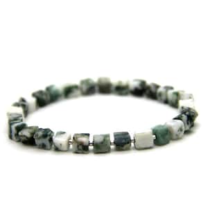 Puede incluir: Un brazalete hecho de cuentas de ágata verde y blanca. Las cuentas son de forma cuadrada y enhebradas en un alambre de plata.