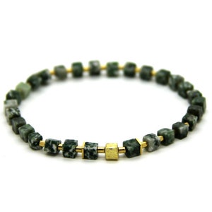 Puede incluir: Un brazalete verde y dorado con cuentas cuadradas. Las cuentas están hechas de una piedra verde con motas blancas y están separadas por separadores dorados.