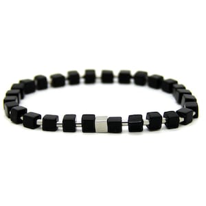 Puede incluir: Un brazalete negro con cuentas cuadradas y un acento plateado.