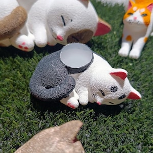 Puede incluir: Tres pequeñas figuritas de gato de cerámica. Un gato blanco está durmiendo con la cabeza apoyada en sus patas. Otro gato blanco está durmiendo con la cabeza apoyada en sus patas. El tercer gato es blanco y negro y está durmiendo con la cabeza apoyada en sus patas.