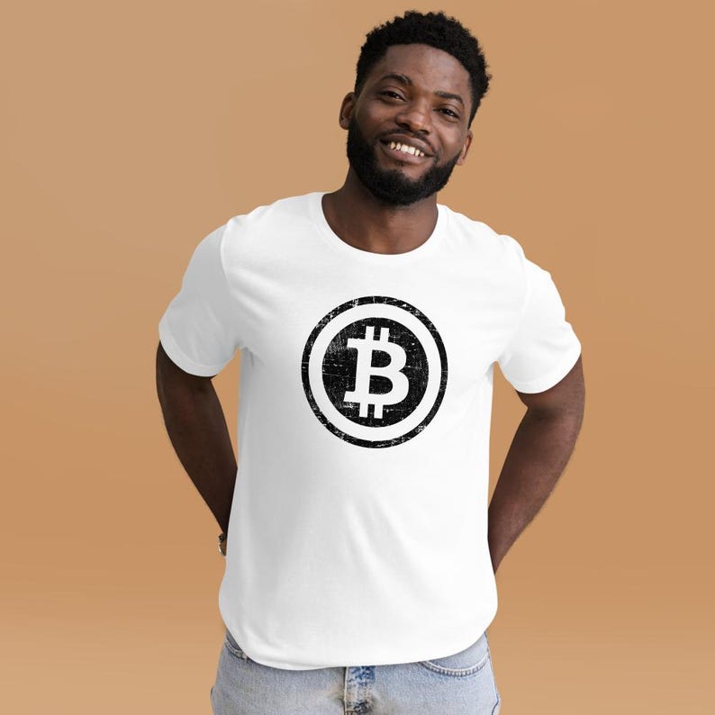 May include: White t-shirt featuring a distressed black Bitcoin symbol. The Bitcoin logo is a stylized letter "B" with vertical lines, enclosed in a circle. The shirt is made of a soft material.