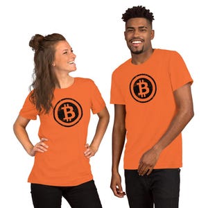 May include: Two people wearing orange t-shirts with a black Bitcoin symbol. The Bitcoin symbol is inside a black circle. The t-shirts are short-sleeved and the people are wearing black pants.
