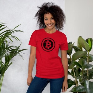May include: A red t-shirt featuring a black Bitcoin symbol. The Bitcoin symbol is a stylized letter "B" with two vertical lines through it, enclosed in a circle. The shirt is made of a soft material and is suitable for casual wear.