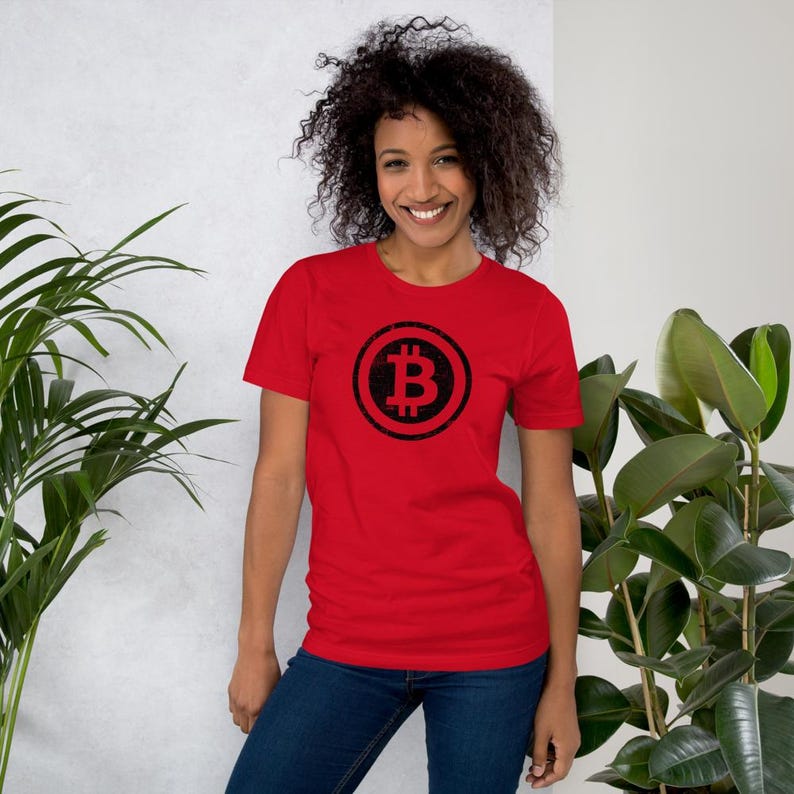 May include: A red t-shirt featuring a black Bitcoin symbol. The Bitcoin symbol is a stylized letter "B" with two vertical lines through it, enclosed in a circle. The shirt is made of a soft material and is suitable for casual wear.