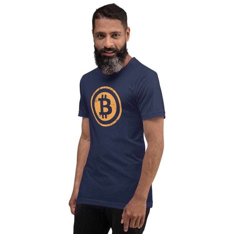 May include: Navy blue t-shirt featuring a distressed gold Bitcoin symbol within a circle. The shirt is made of a soft material and has short sleeves. The Bitcoin symbol is centered on the chest.