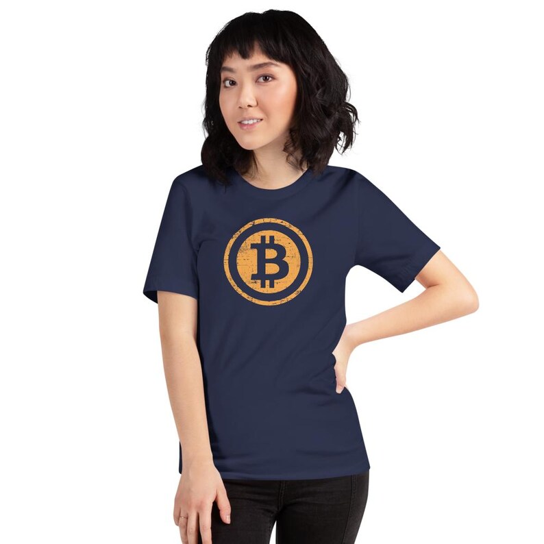 May include: A navy blue t-shirt featuring a Bitcoin symbol in a distressed, gold-colored circle. The Bitcoin logo is centered on the chest. The shirt is short-sleeved and made of a soft material.