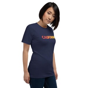 Op de afbeelding: Marineblauw T-shirt met het woord "CALIFORNIA" in een oranje en gele gradi&euml;nt. Het T-shirt heeft een ronde hals en korte mouwen.