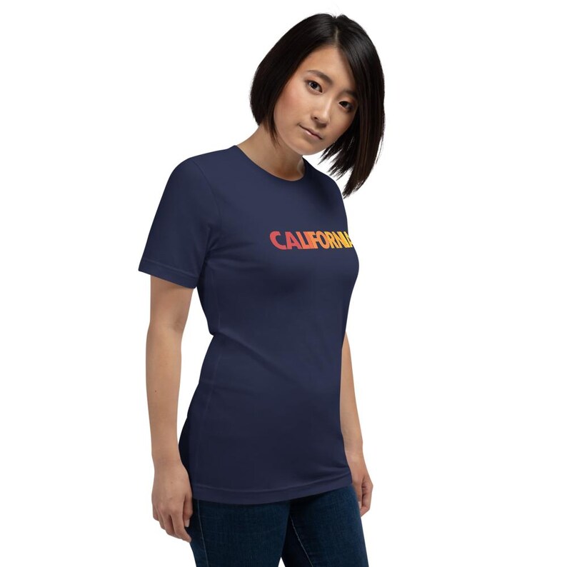 Op de afbeelding: Marineblauw T-shirt met het woord "CALIFORNIA" in een oranje en gele gradi&euml;nt. Het T-shirt heeft een ronde hals en korte mouwen.