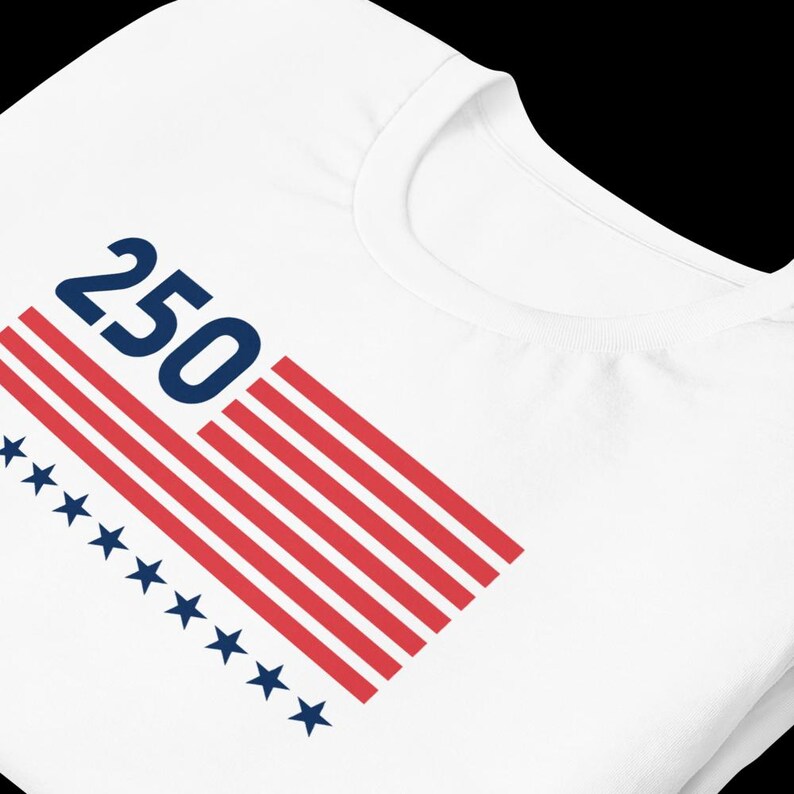 K&ouml;nnte beinhalten: Wei&szlig;es T-Shirt mit einem stilisierten amerikanischen Flaggen-Design. Die Flagge zeigt rote und wei&szlig;e Streifen, blaue Sterne und die Zahl "250" in Marineblau, wahrscheinlich zur Erinnerung an ein Jubil&auml;um oder einen Meilenstein.