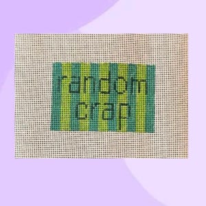 Może przedstawiać: Płótno do haftu krzyżykowego ze słowami "random crap" wyszytymi na czarno na zielono-turkusowym tle w paski. Płótno jest umieszczone na jasnofioletowym tle.