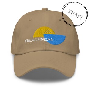 Może przedstawiać: Bejsbolówka w kolorze khaki z haftowanym logo przedstawiającym żółte słońce i niebieską wodę z napisem "REACHPEAK" w kolorze białym.