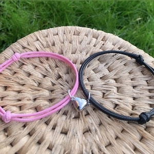 May include: Two friendship bracelets with heart charms. One bracelet is pink and the other is black.