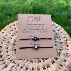 May include: Two black friendship bracelets with the letters "K" and "P" on them. The bracelets are on a card with the text "No matter where we go, No matter what we do, You'll always be there for me And I'll always be there for you. One for you One for me"