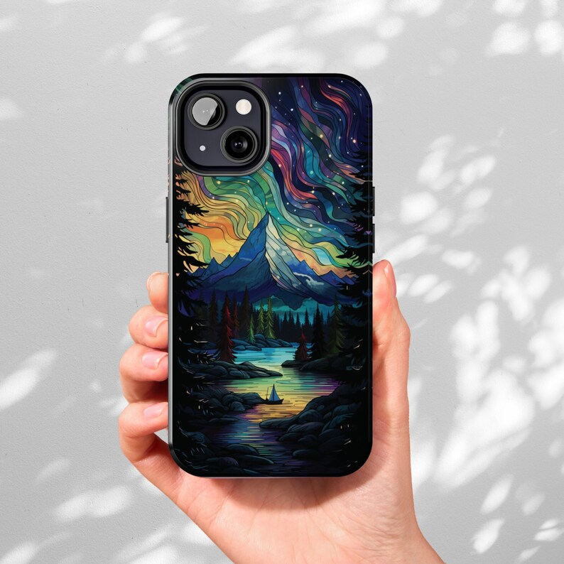 May include: A black iPhone case with a colorful stained glass design of a mountain range, a lake, and a sailboat. The design features a blue, green, yellow, and purple color scheme.