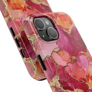 Pu&ograve; includere: Una custodia per telefono rosa e arancione con un motivo a marmi e dettagli dorati. La custodia ha un rialzo per la fotocamera e un ritaglio per i pulsanti del telefono.