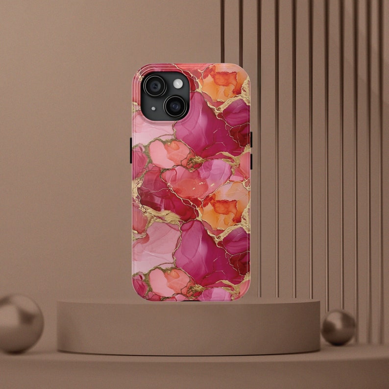 Pu&ograve; includere: Una custodia per telefono rosa e oro con un motivo floreale e un ritaglio per la fotocamera. La custodia ha un design marmoreo con accenti rosa, rosso e oro.