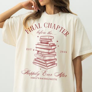 May include: Ivory-colored t-shirt with the text "FINAL CHAPTER before the..." in burgundy script. A stack of books is centered below the text, with the words "Happily Ever After" and "Emily's Bachelorette" below the books. The year "2026" is also printed on the shirt.