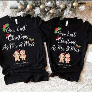 Op de afbeelding: Twee zwarte t-shirts met korte mouwen voorzien van de witte tekst Our Last Christmas As Mr & Miss, versierd met hulst, een kerstmuts en twee peperkoekfiguurtjes. Onder de figuren staan de namen Emma & Jamie en het jaartal 2026 gedrukt.