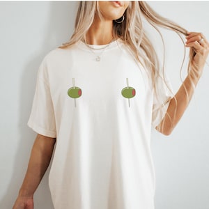 May include: A white t-shirt with a graphic of two green olives on toothpicks.