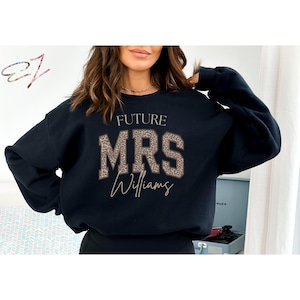May include: Black sweatshirt with the text "FUTURE MRS Williams" in a leopard print design. The sweatshirt is a crew neck style and is likely made of a soft material. The design is centered on the front.