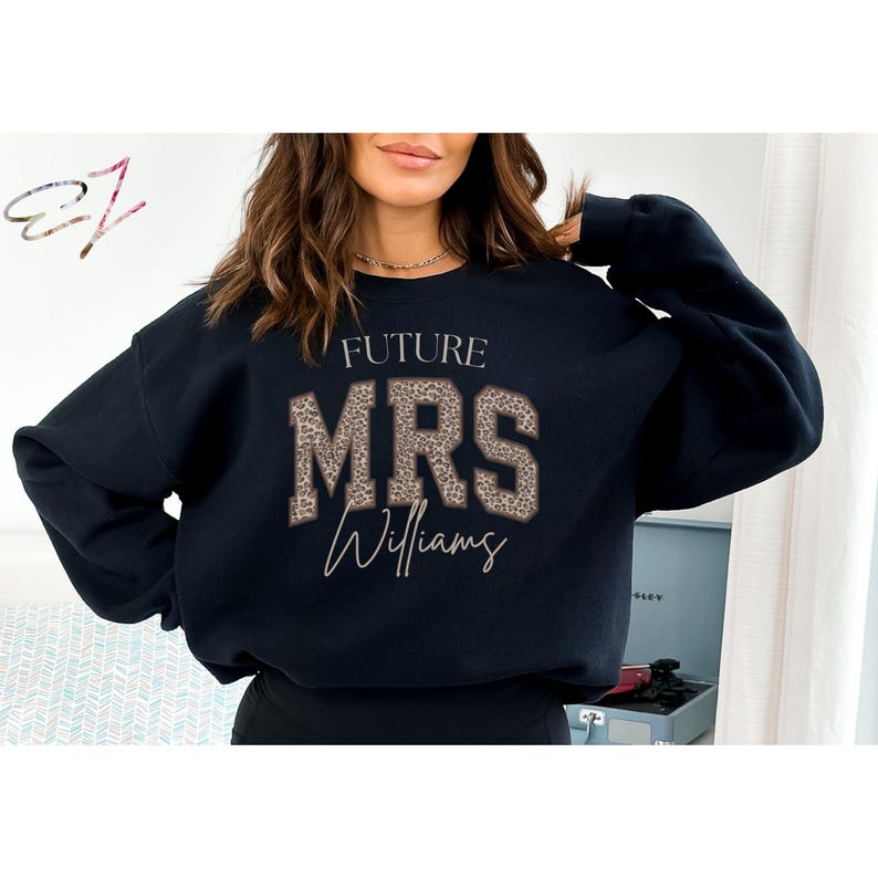 May include: Black sweatshirt with the text "FUTURE MRS Williams" in a leopard print design. The sweatshirt is a crew neck style and is likely made of a soft material. The design is centered on the front.