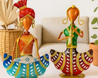 May include: Two decorative metal figurines of musicians. One wears a red turban and orange clothing, holding a blue drum. The other plays a horn and wears a green top and red skirt. Both have gold accents.