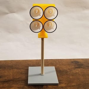 May include: A yellow plastic model of a traffic light with four round white lights on a wooden pole and a gray base.