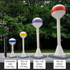 May include: Four white water tower models of varying sizes, each with a colored band at the top: blue, yellow, purple, and red. The smallest is 5.8 inches tall, the largest is 15.6 inches tall. Each sits on a gray square base.