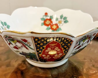 May include: A white porcelain bowl with a scalloped rim and a gold trim. The bowl is decorated with a floral pattern in red, green, and gold, and a bird pattern in blue, green, and gold.