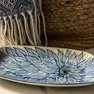 Puede incluir: Un plato de servir de cerámica blanca con un diseño floral azul y amarillo. El plato tiene forma ovalada y tiene un borde elevado.
