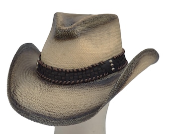 Puede incluir: Sombrero de vaquero de paja tejida en tonos beige y gris. Cuenta con una banda de cuero marrón oscuro con tachuelas plateadas. El ala es curvada. El sombrero se muestra sobre una superficie blanca.