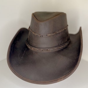 Pode incluir: Um chap&eacute;u de cowboy de couro marrom com uma faixa de couro tran&ccedil;ada ao redor da coroa.