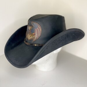 May include: A black leather cowboy hat with a brown leather eagle design on the crown. The eagle has a red, white and blue design on its wings.
