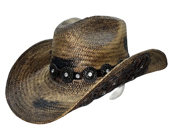 Pode incluir: Um chapéu de cowboy de palha marrom e preto com uma faixa de couro marrom e strass. O chapéu tem uma aba larga e uma coroa pontiaguda.
