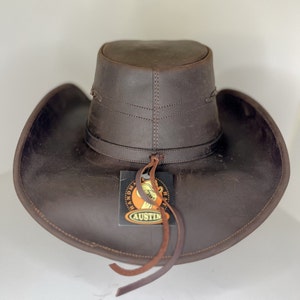 Pode incluir: Um chap&eacute;u de cowboy de couro marrom com uma aba larga e uma faixa de couro. O chap&eacute;u tem uma etiqueta que diz "Handmade Hats Austin".
