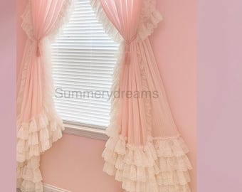 May include: A pair of light pink curtains featuring a ruffled top header and multiple layers of white lace trim along the edges. The curtains are tied back with matching pink tassels and feature the text Summerdreams printed in the centre.
