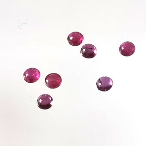 Könnte beinhalten: Sieben runde, rosafarbene, facettierte Edelsteine auf einer weißen Oberfläche.