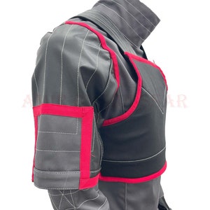 May include: A black and gray padded vest with red trim. The vest has a high collar and a zipper closure. The vest is made of a durable material and is designed for protection.