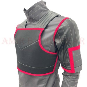 May include: A black vest with red trim, worn over a gray shirt. The vest has a padded front and a strap across the chest.