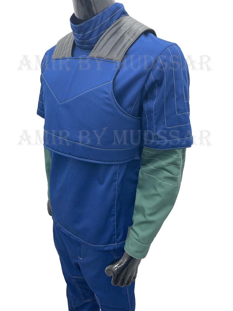 May include: A blue jumpsuit with a black vest and a green undershirt. The vest has a padded front and a black strap across the shoulders. The jumpsuit has white stitching details.