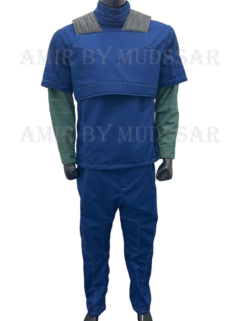 May include: A blue jumpsuit with a dark blue vest and a high collar. The vest has a padded chest piece and shoulder straps. The jumpsuit has a zipper in the front and pockets on the legs.